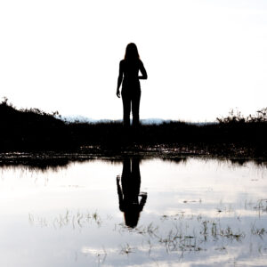 Silhouette of woman reflected in a mountain lake